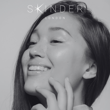 Load image into Gallery viewer, a soft black and white image of a woman with clear, bright, glowing skin. she looks happy. the SKINDER LONDON logo is at the top of the screen. @skinderofficial